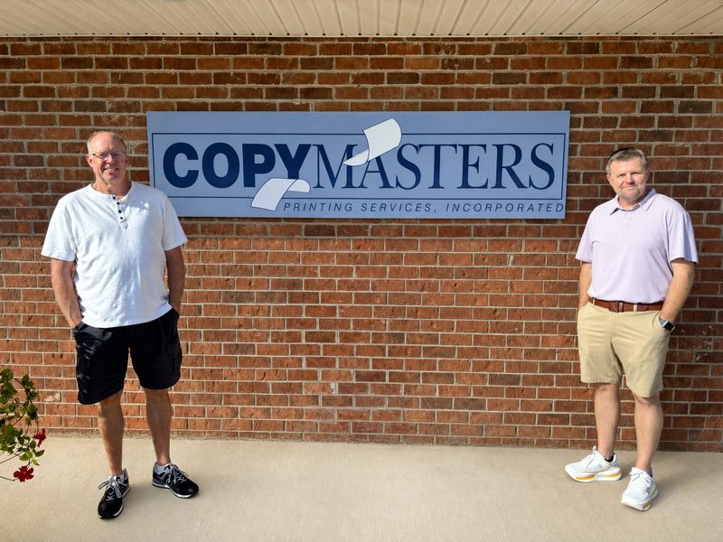 Jimmy and Billy outside the shop, under the CopyMasters sign on the brick wall